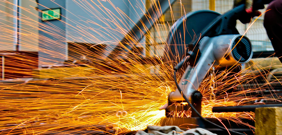 A person using a circular saw to cut metal, with bright orange sparks flying in all directions, set in an industrial environment.